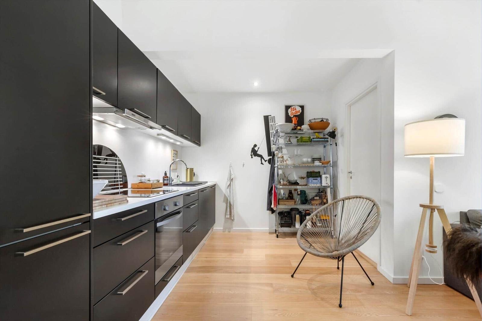 Kitchen with black cabinets and wooden floor. Metal shelf and chair in the background.