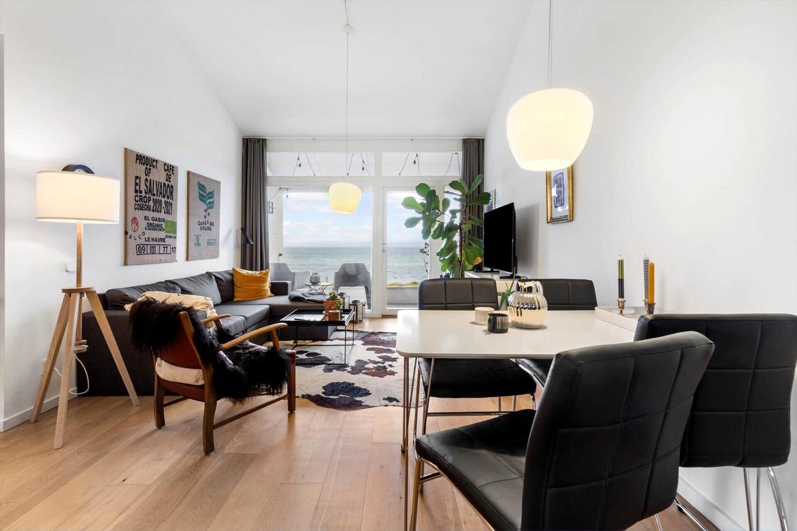 Living and dining area with sea view, sofa, dining table, and plants.