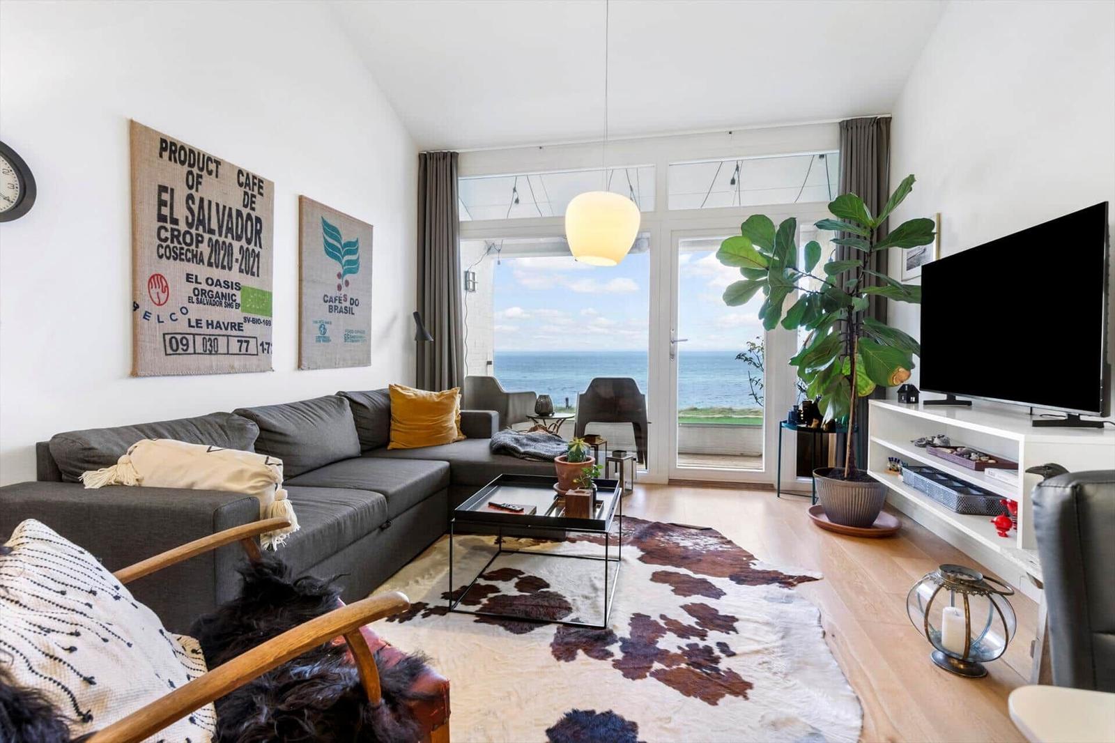 Living room with sofa, TV, and ocean view through glass door.