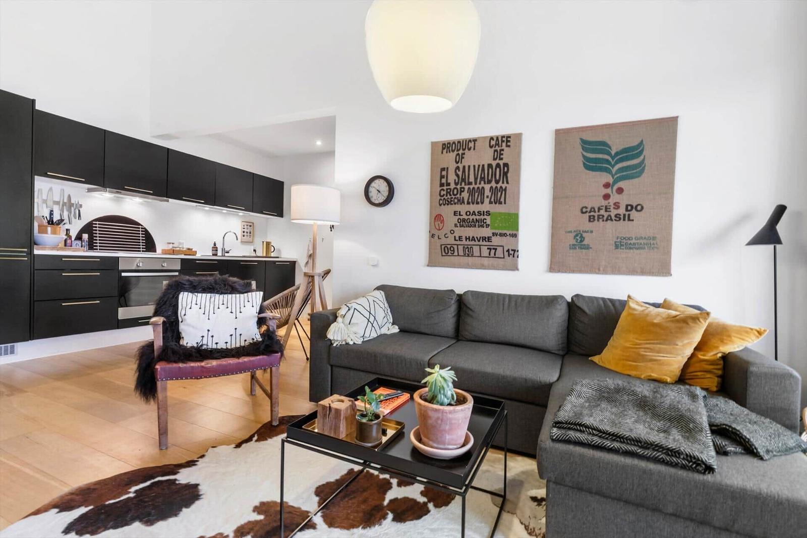 Living area with sofa, coffee table, and kitchen. Wall decor and wooden floor.