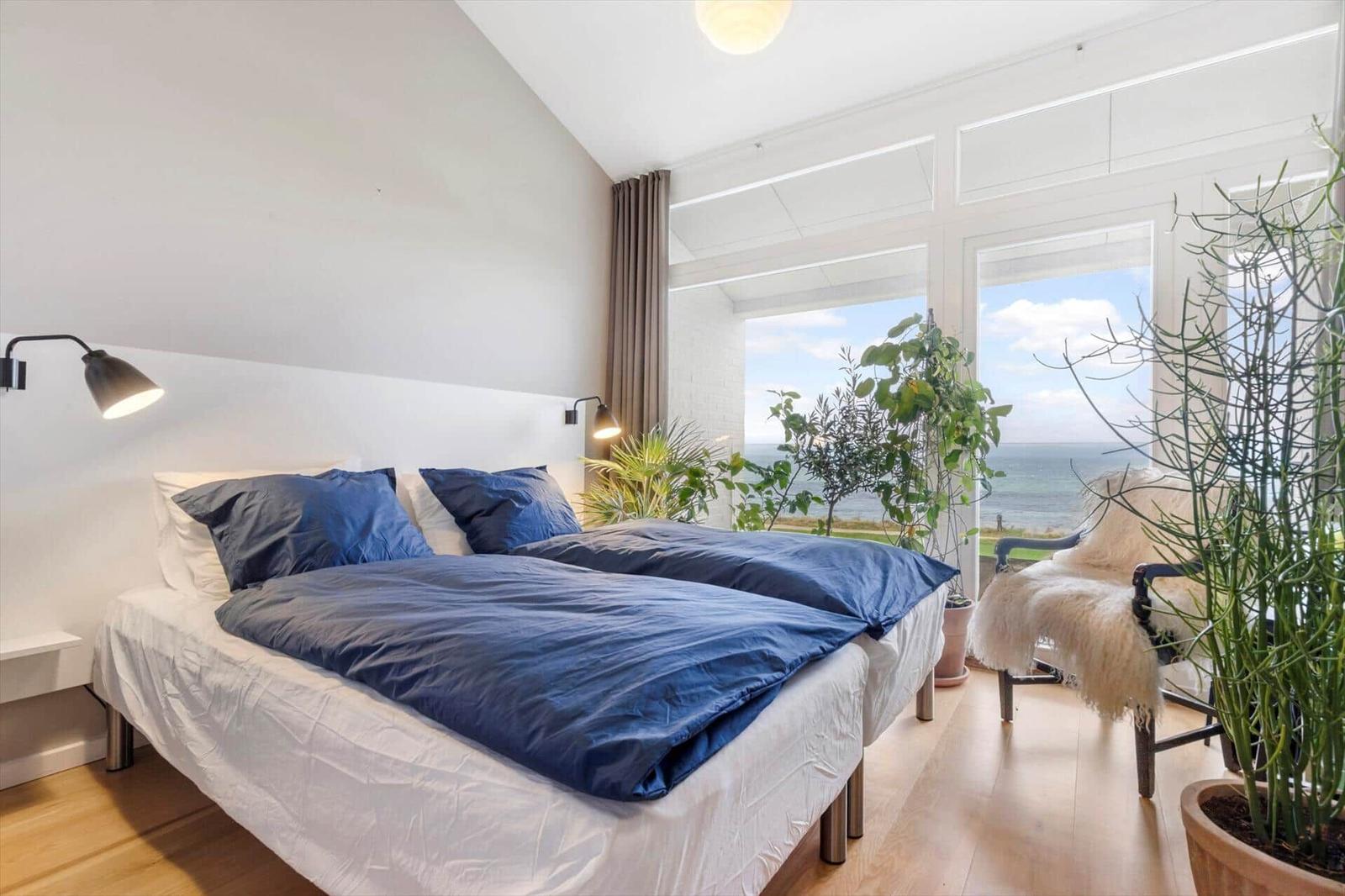 Bedroom with bed, sea view through windows, and plants
