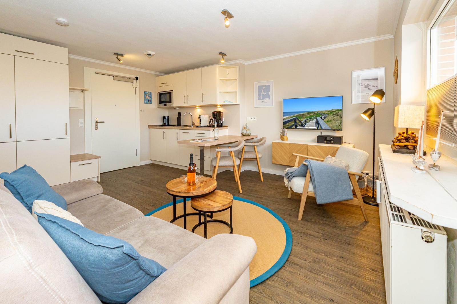 Wohnung mit Küche, Wohnbereich und Fernseher. Holzboden und moderne Einrichtung.