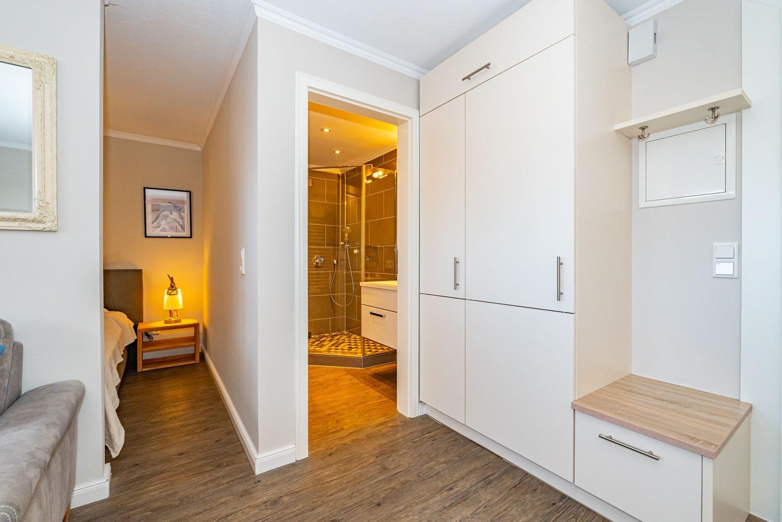 Flur mit Schlafzimmer und Bad. Weiße Schränke, Holzboden und Spiegel.