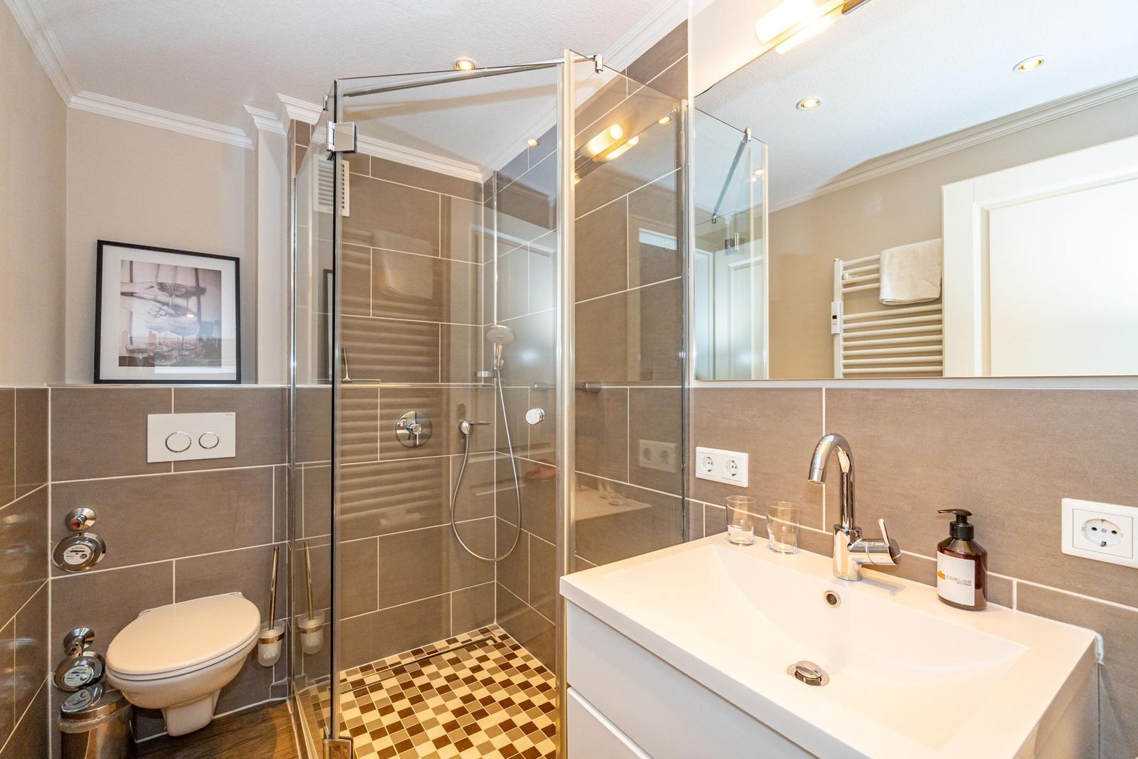 Badezimmer mit Dusche, Waschbecken und Toilette. Fliesenwand und Spiegel.