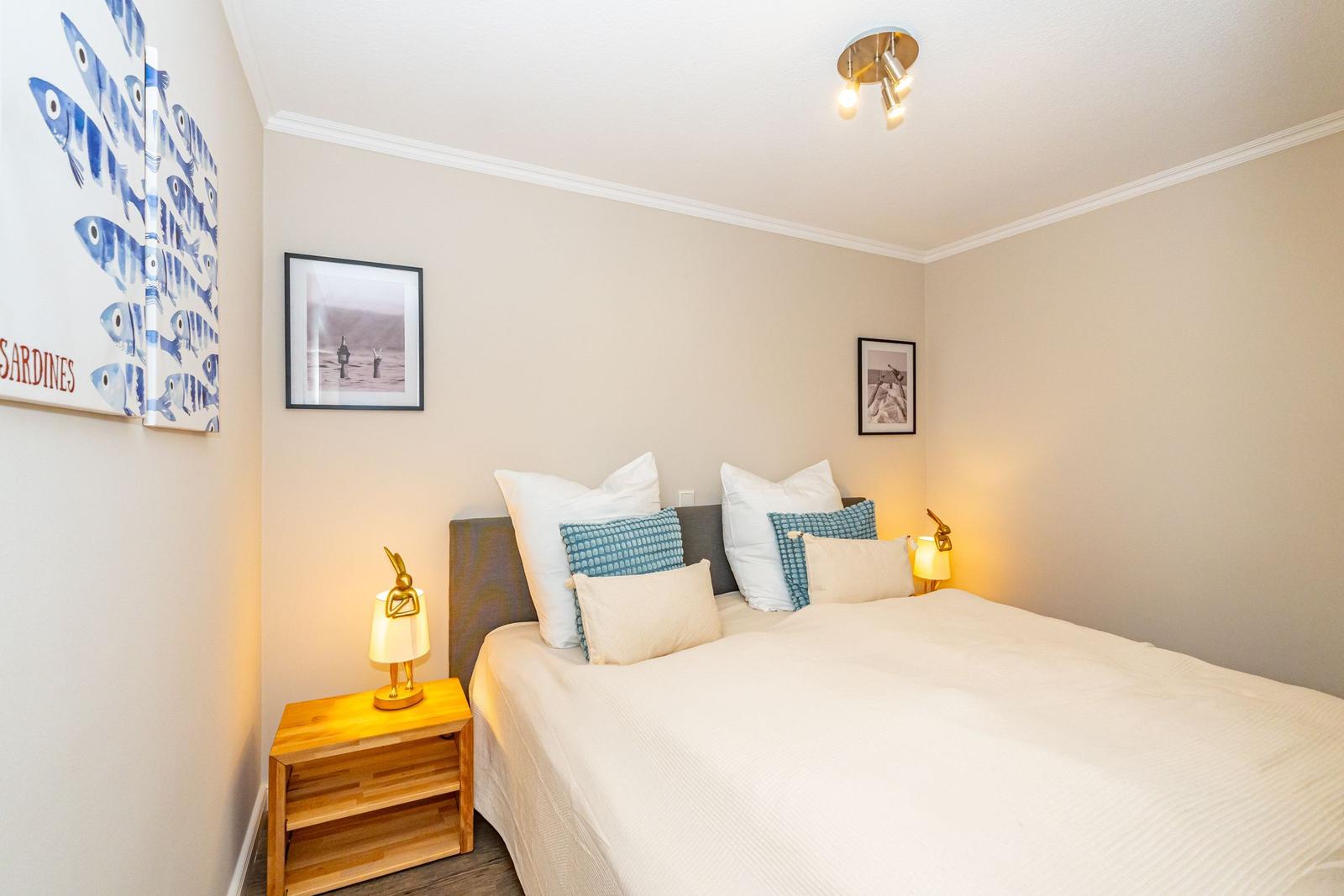 Schlafzimmer mit Bett, Nachttisch und Wandbildern.