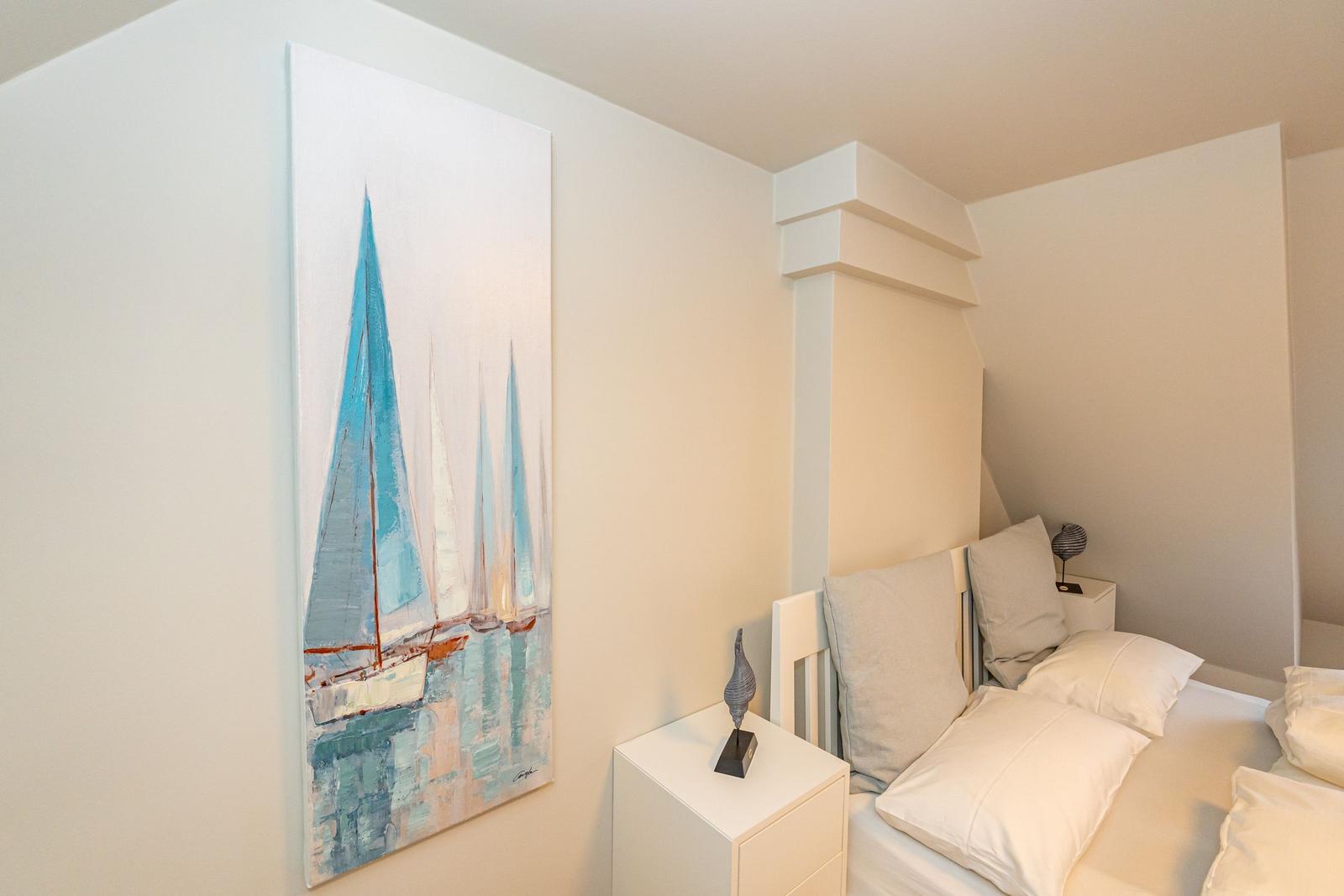 Schlafzimmer mit Bett, Nachttisch und Wandbild mit Segelbooten.