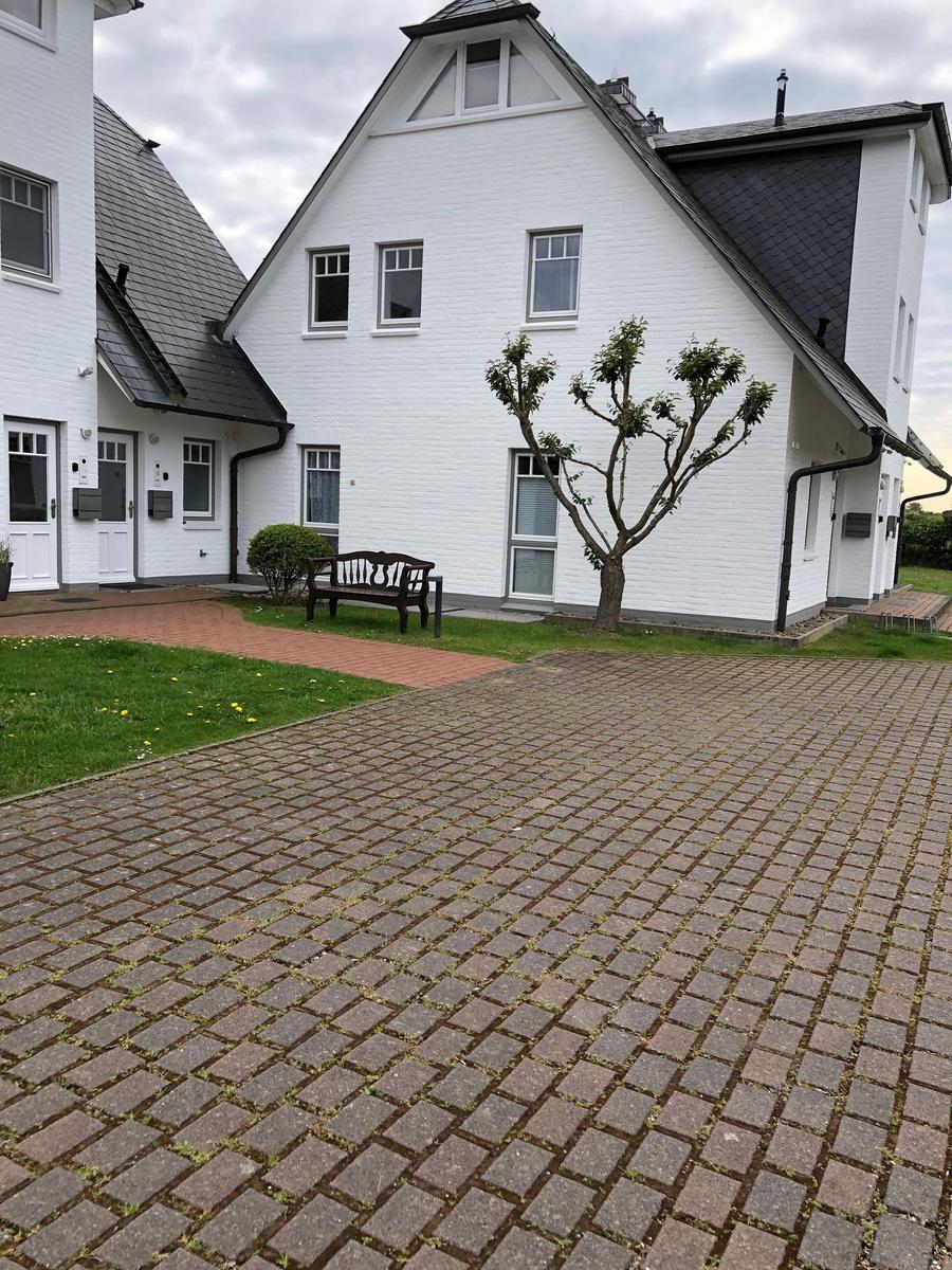 Weiße Villa mit gepflastertem Hof und Gartenbereich mit Bank und Baum.