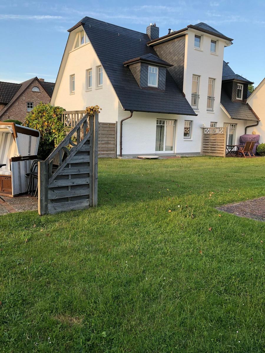 Haus mit Garten, Terrasse und Holzgeländer. Grünfläche und Sitzgelegenheiten.