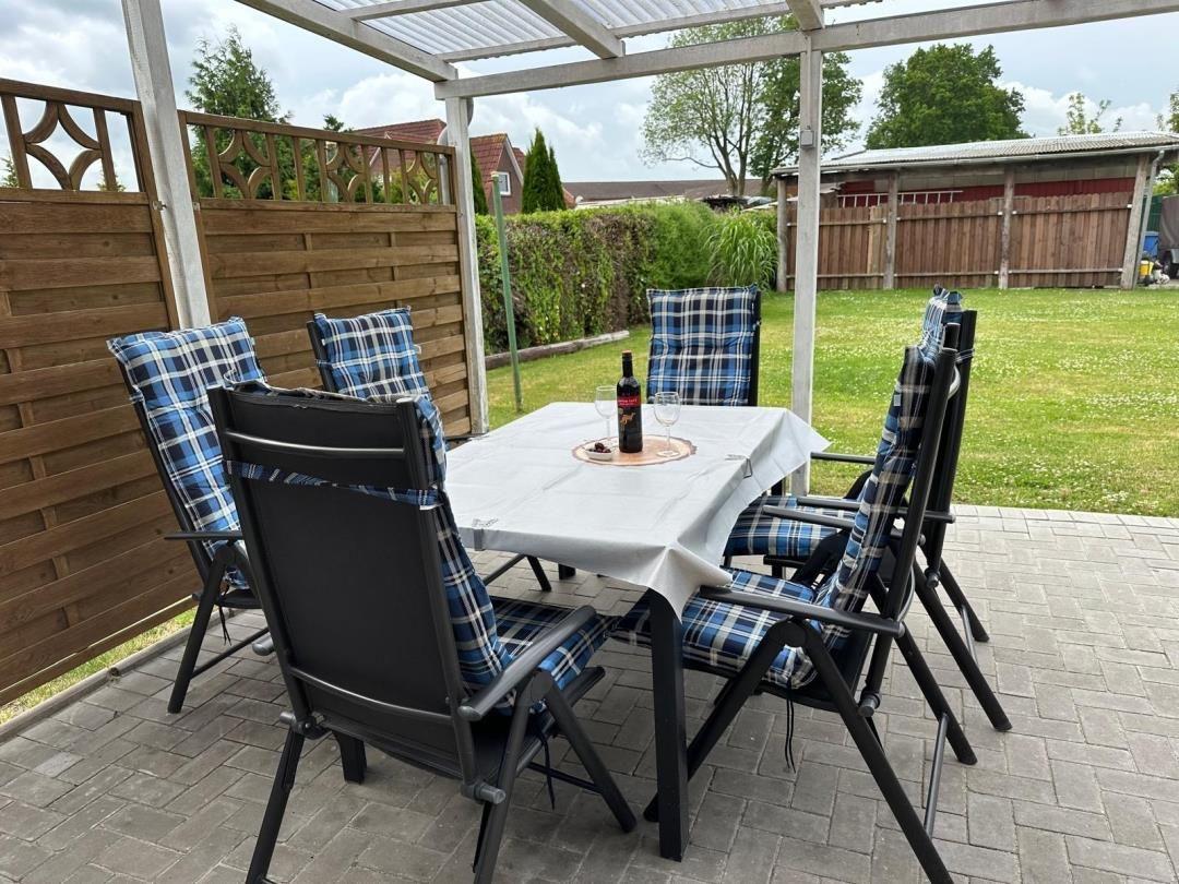 Terrasse mit gedecktem Tisch und sechs Stühlen unter einer Markise.