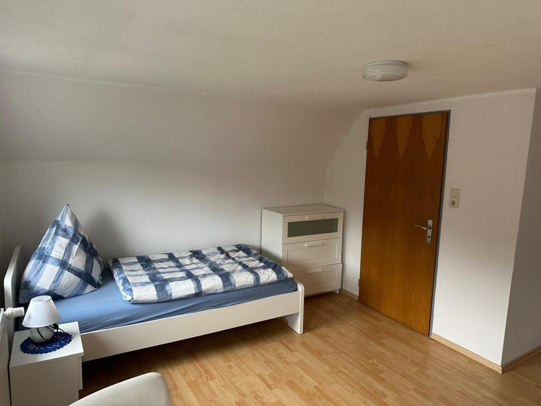 Ein Schlafzimmer mit Einzelbett, Nachttisch und Schrank. Holzfußboden und Holztür.