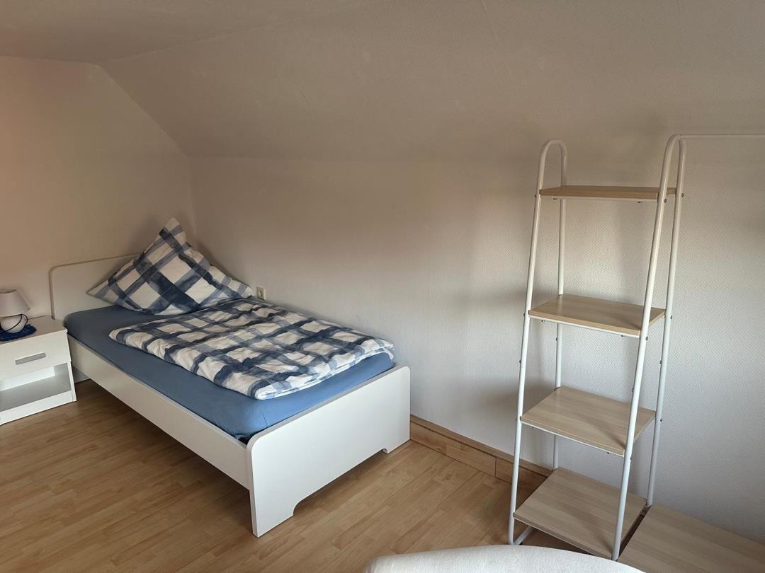 Ein Schlafzimmer mit Einzelbett, Nachttisch und Regal. Holzfußboden und schräge Decke.
