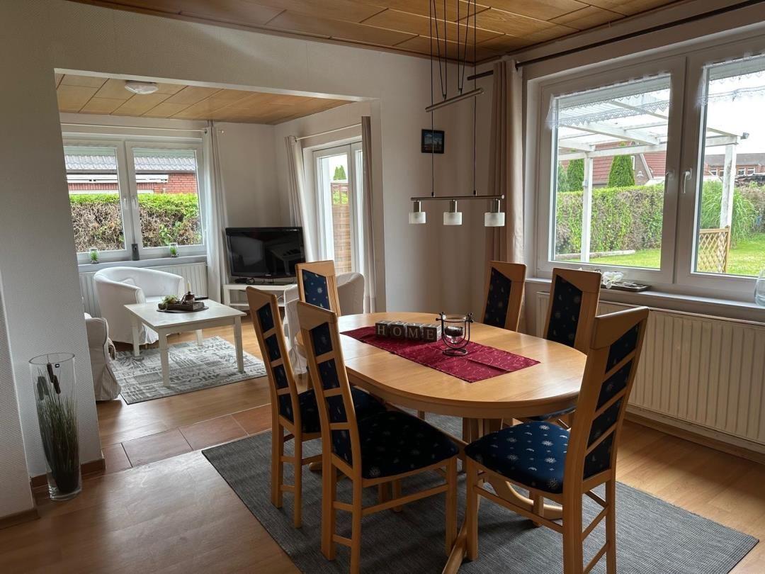 Esszimmer mit runden Tisch und Stühlen. Wohnzimmer im Hintergrund mit TV und Fenster.