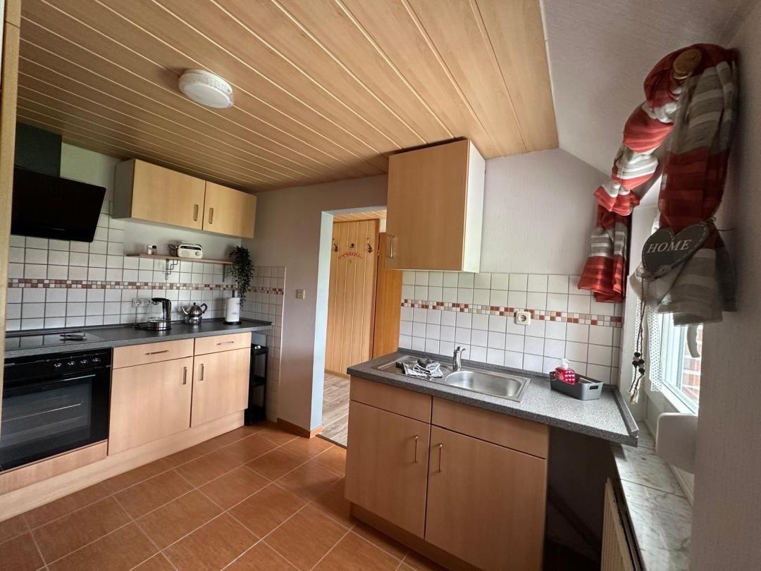 Küche mit Holzregalen, Spüle und Herd. Fenster mit Schal und Herz.