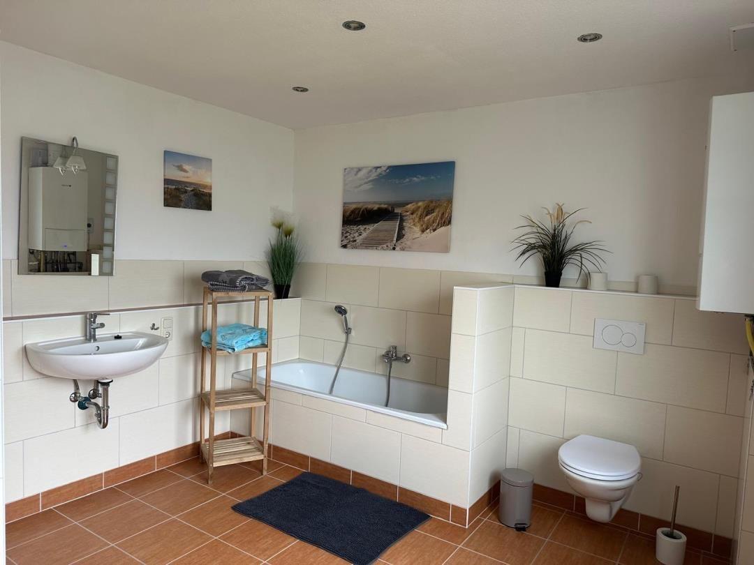 Badezimmer mit Badewanne, Waschbecken und Toilette. Wandbilder und Pflanzen.