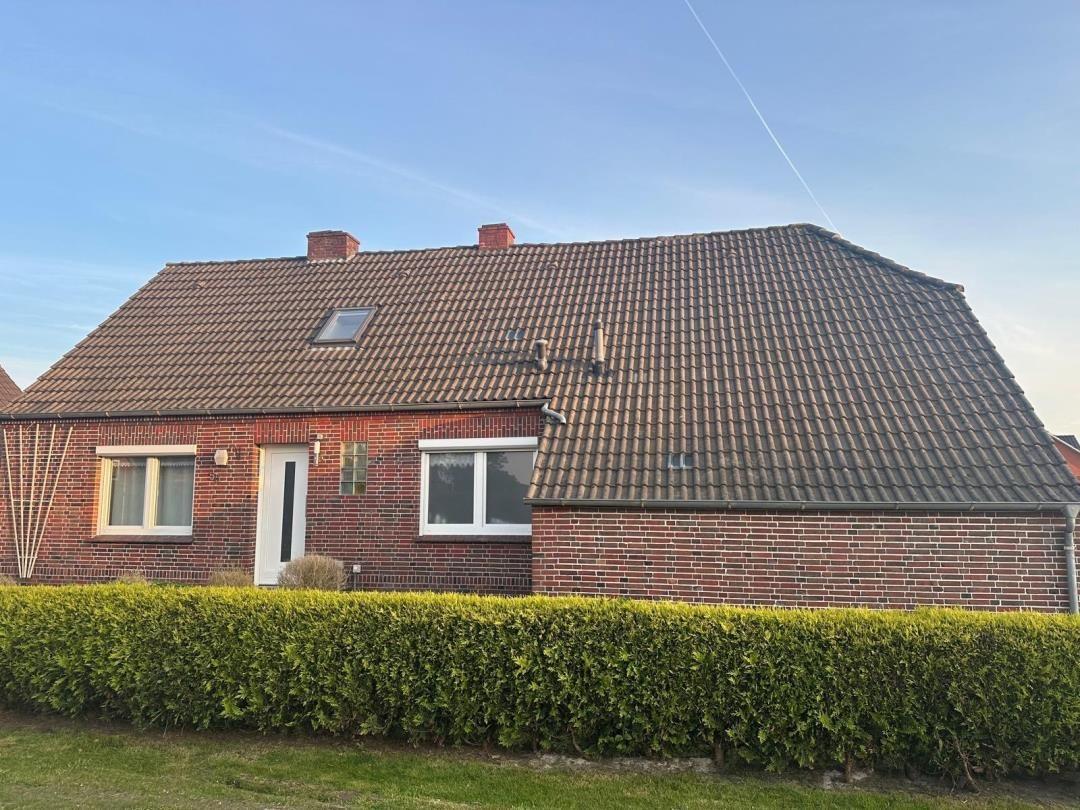 Einfamilienhaus mit Ziegeldach, rotem Backstein und grüner Hecke im Vorgarten.