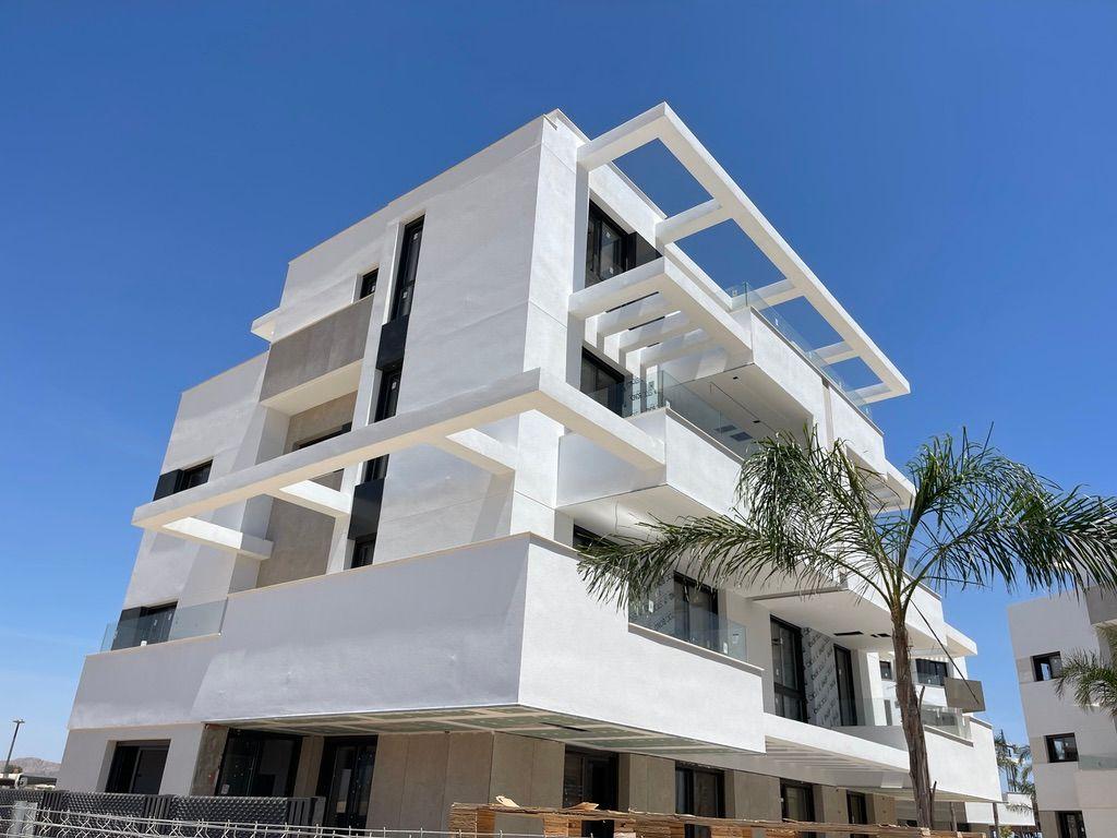 Modern white building with balconies and glass railings under blue sky.
