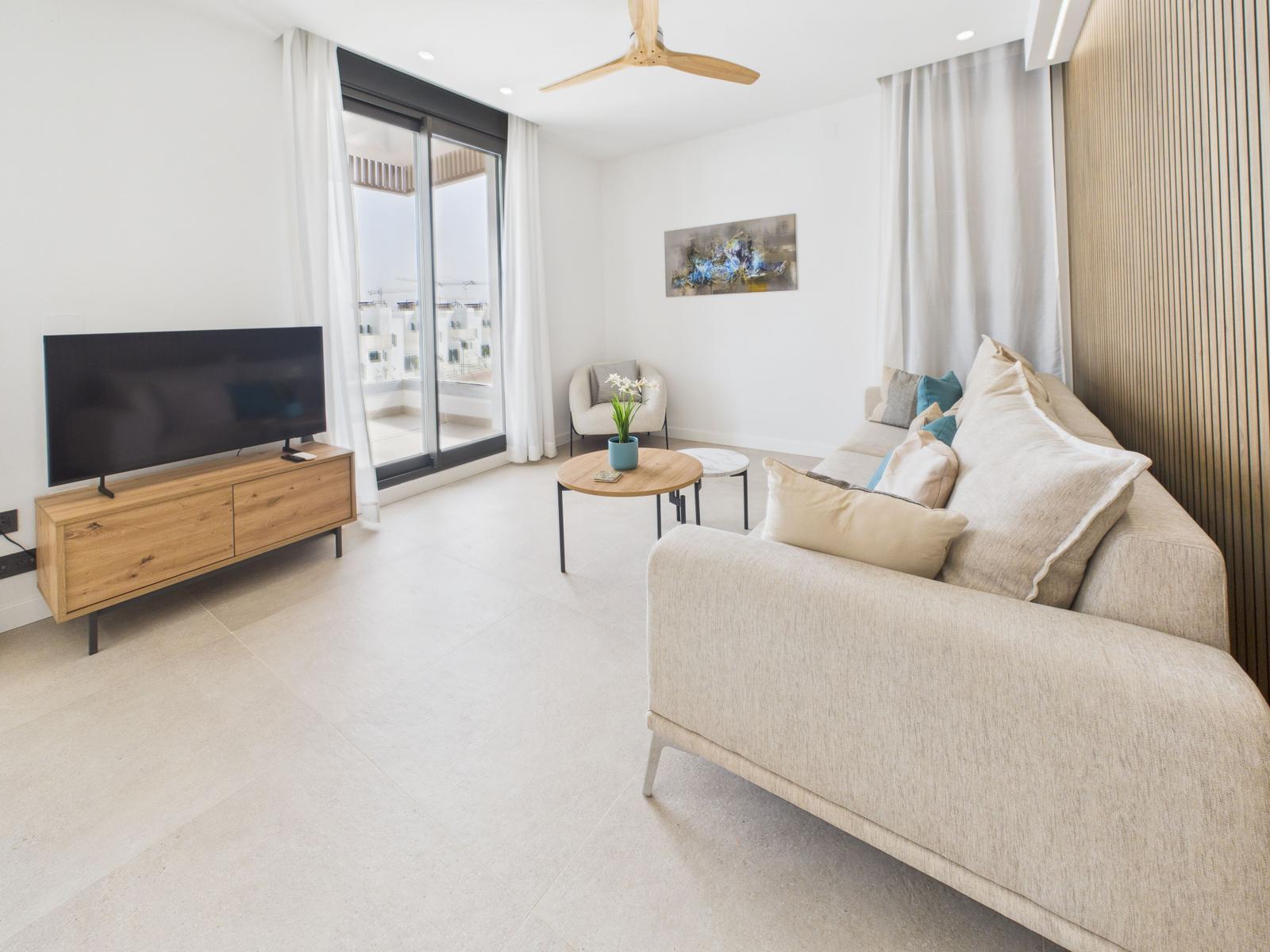 Living room with sofa, TV, and balcony view. Modern furnishings with wooden elements.