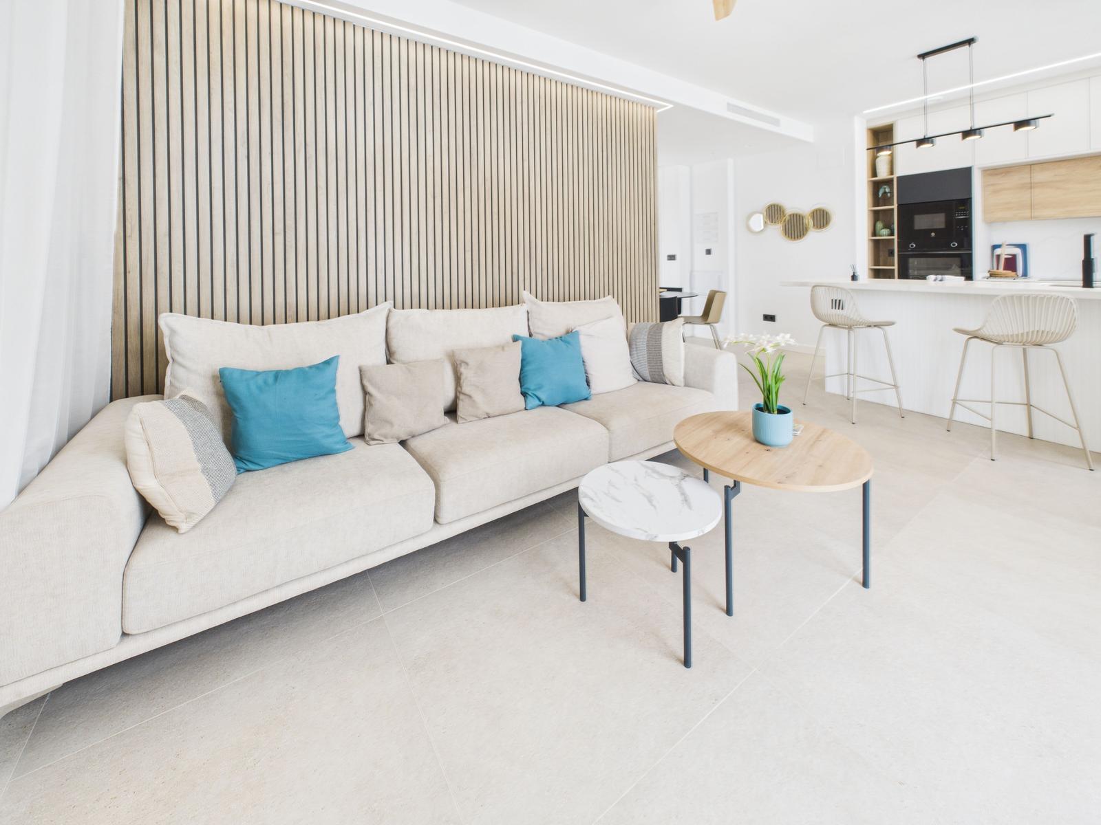 Living room with sofa, tables, and kitchen area in background.