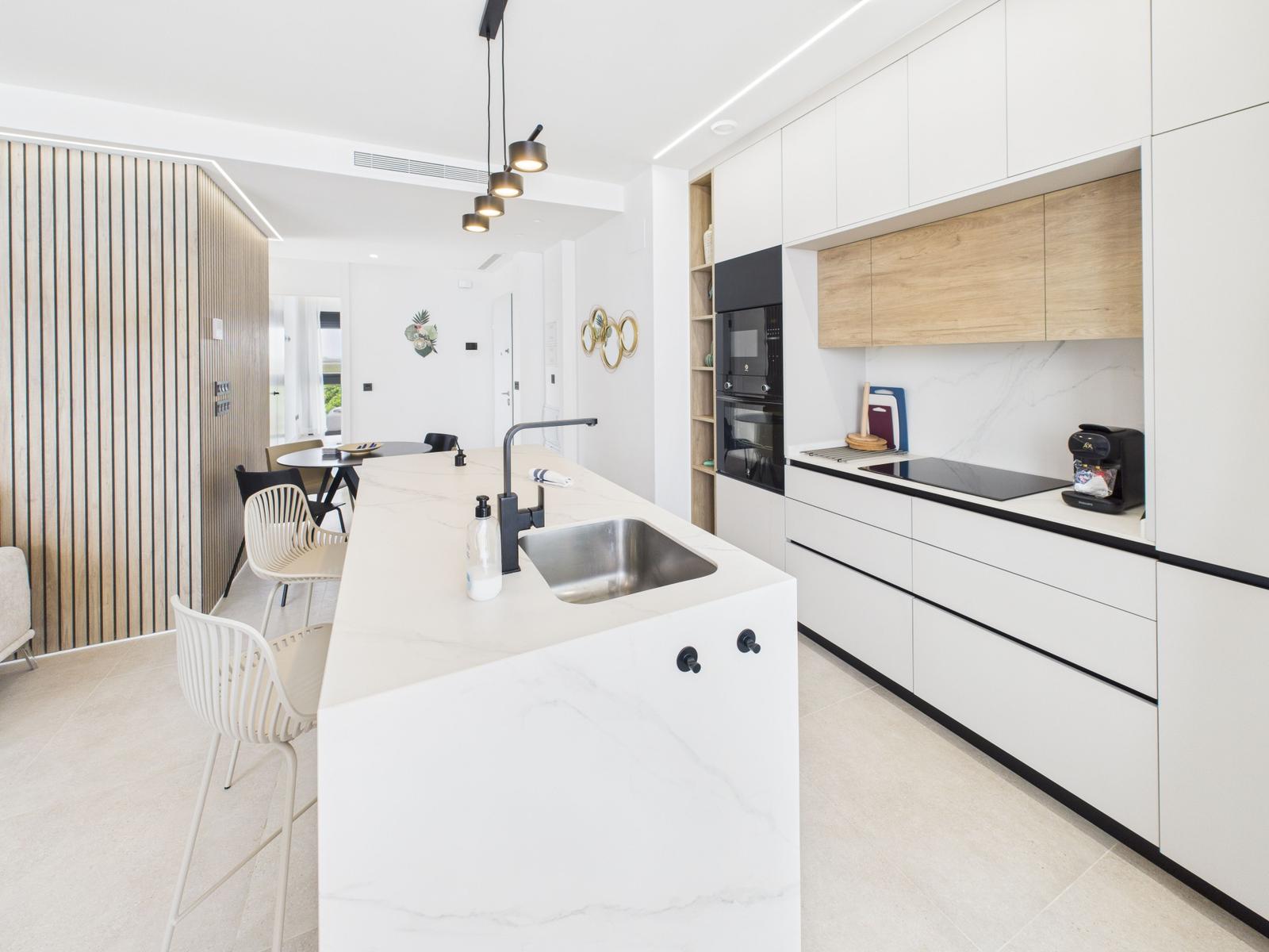 Modern kitchen with island, stainless steel sink, and white cabinets. Dining area in background.