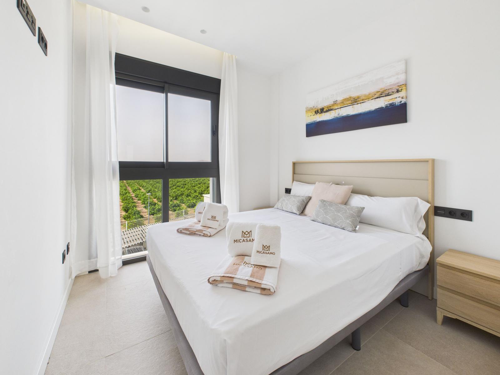 Bedroom with large bed, view of vineyard through window, and modern wall decor.