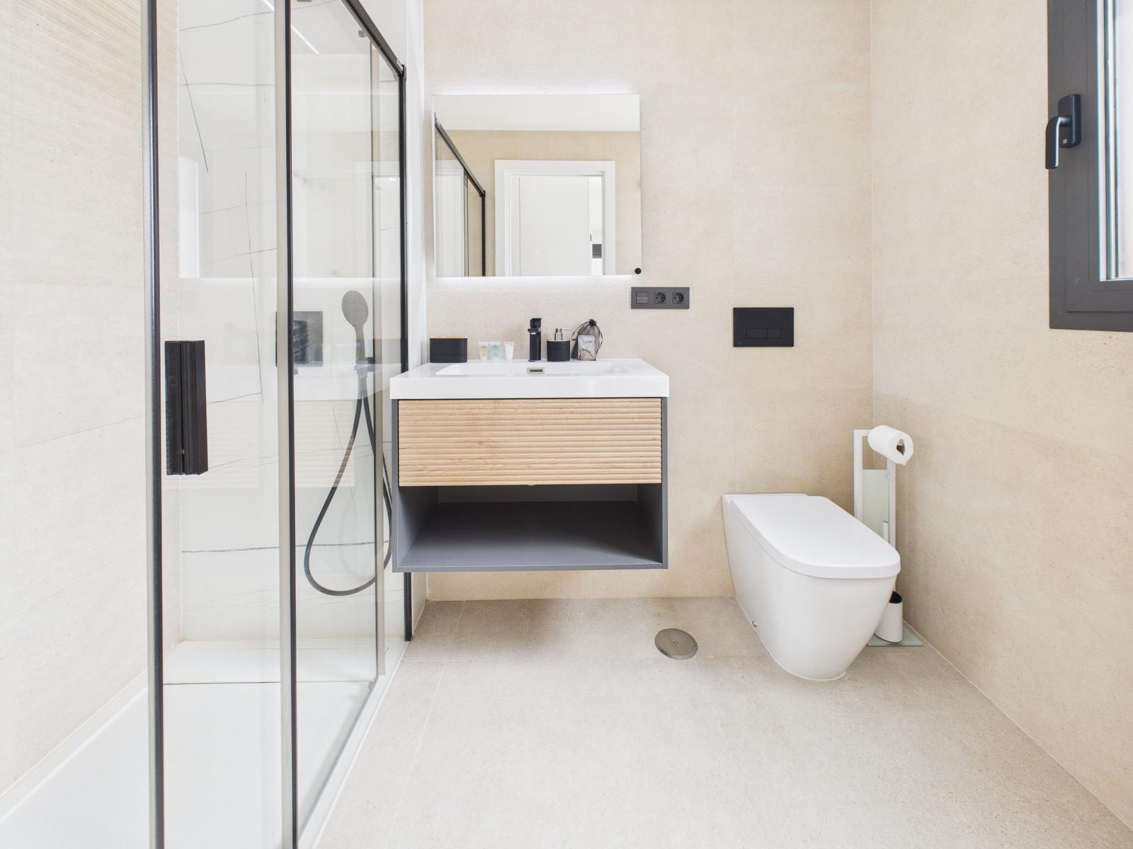 Modern bathroom with shower, sink and toilet. Wall tiles and wooden accents.
