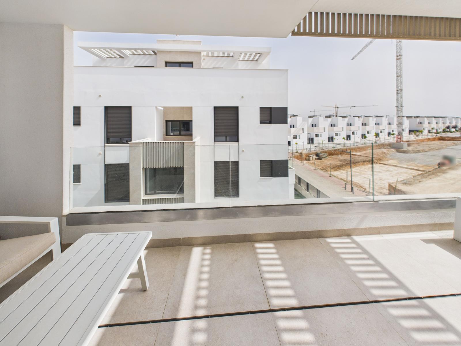 Terrace with white table and bench. View of modern buildings and construction site.