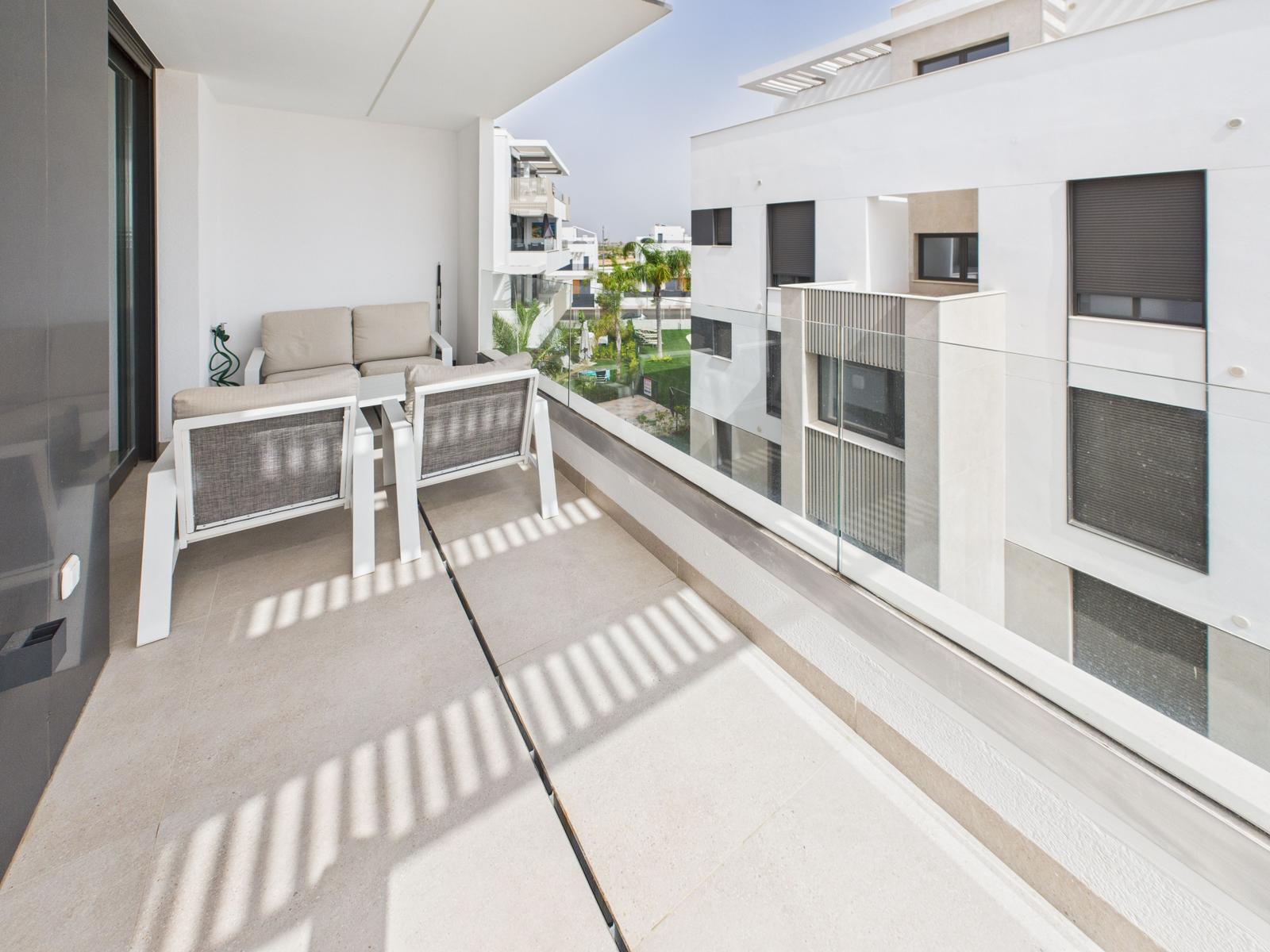 Terrace with seating and glass railing. View of modern buildings and green areas.