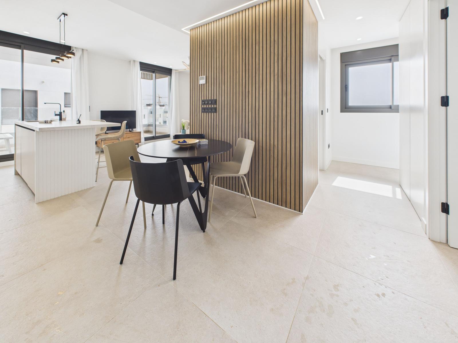Dining area with round table and chairs next to kitchen island and wood panel.