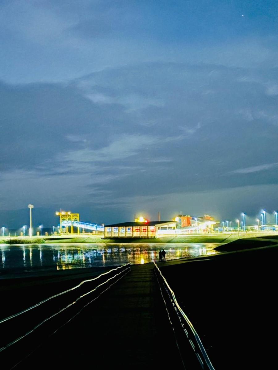 Nachtansicht eines beleuchteten Hafens mit Pier und Reflexionen im Wasser.