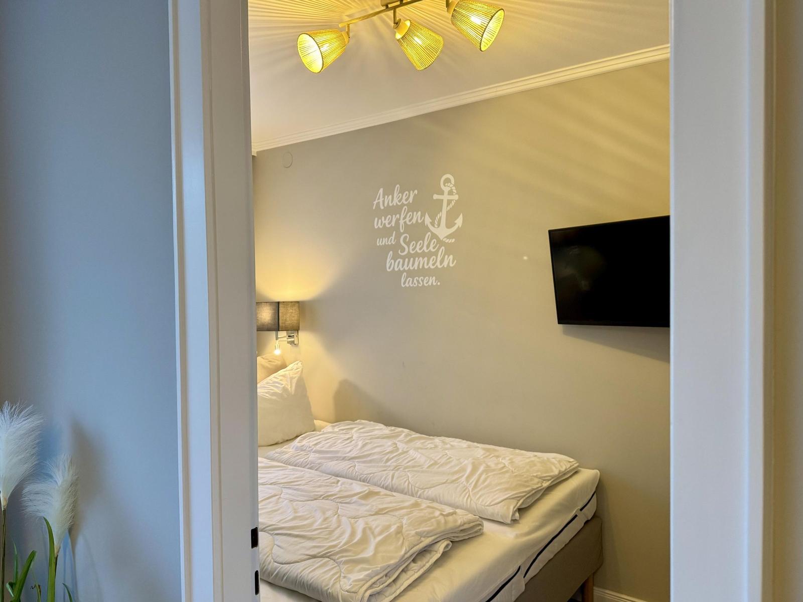 Schlafzimmer mit Bett, Wandtattoo und Wand-TV.