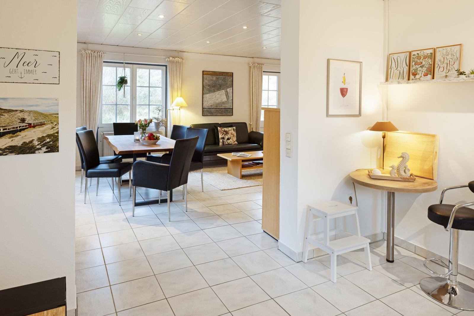 Wohn- und Essbereich mit Tisch, Stühlen und Sofa. Wandbild und Lampen sichtbar.