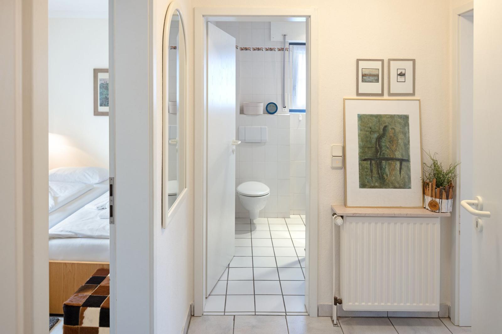 Flur mit Schlafzimmer und Bad. Bad mit Toilette und Dusche. Wandbild und Pflanze.