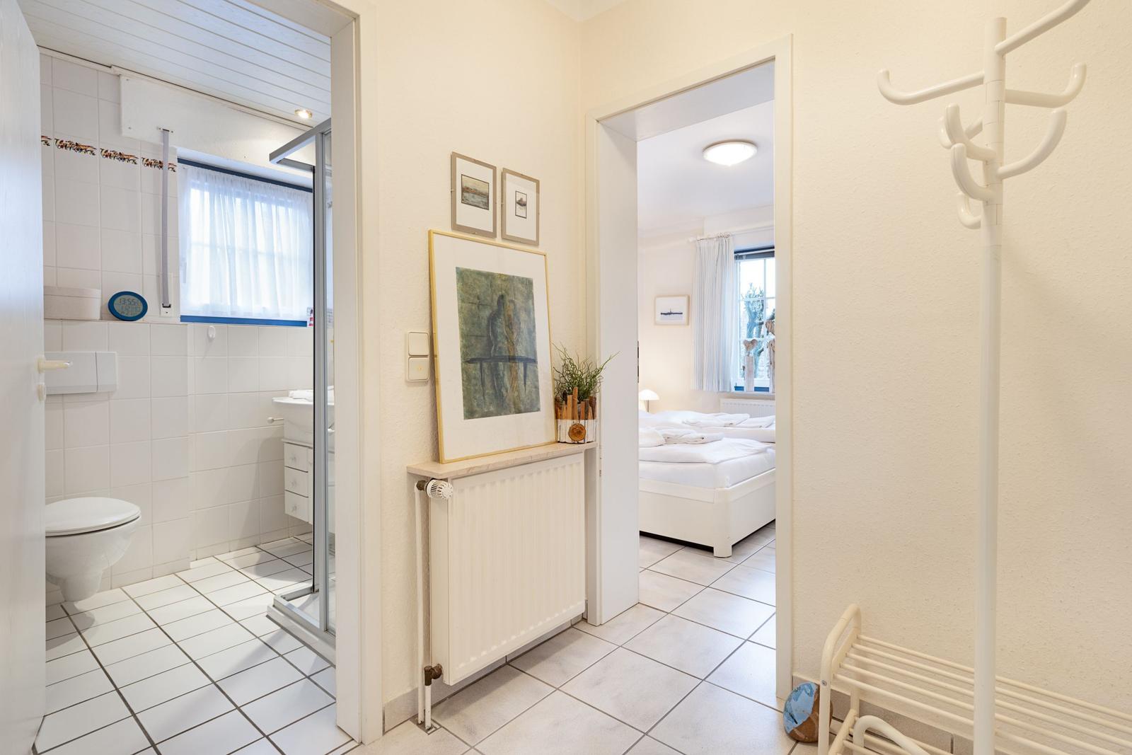 Badezimmer und Schlafzimmer sind über einen Flur erreichbar. An der Wand hängen Bilder.