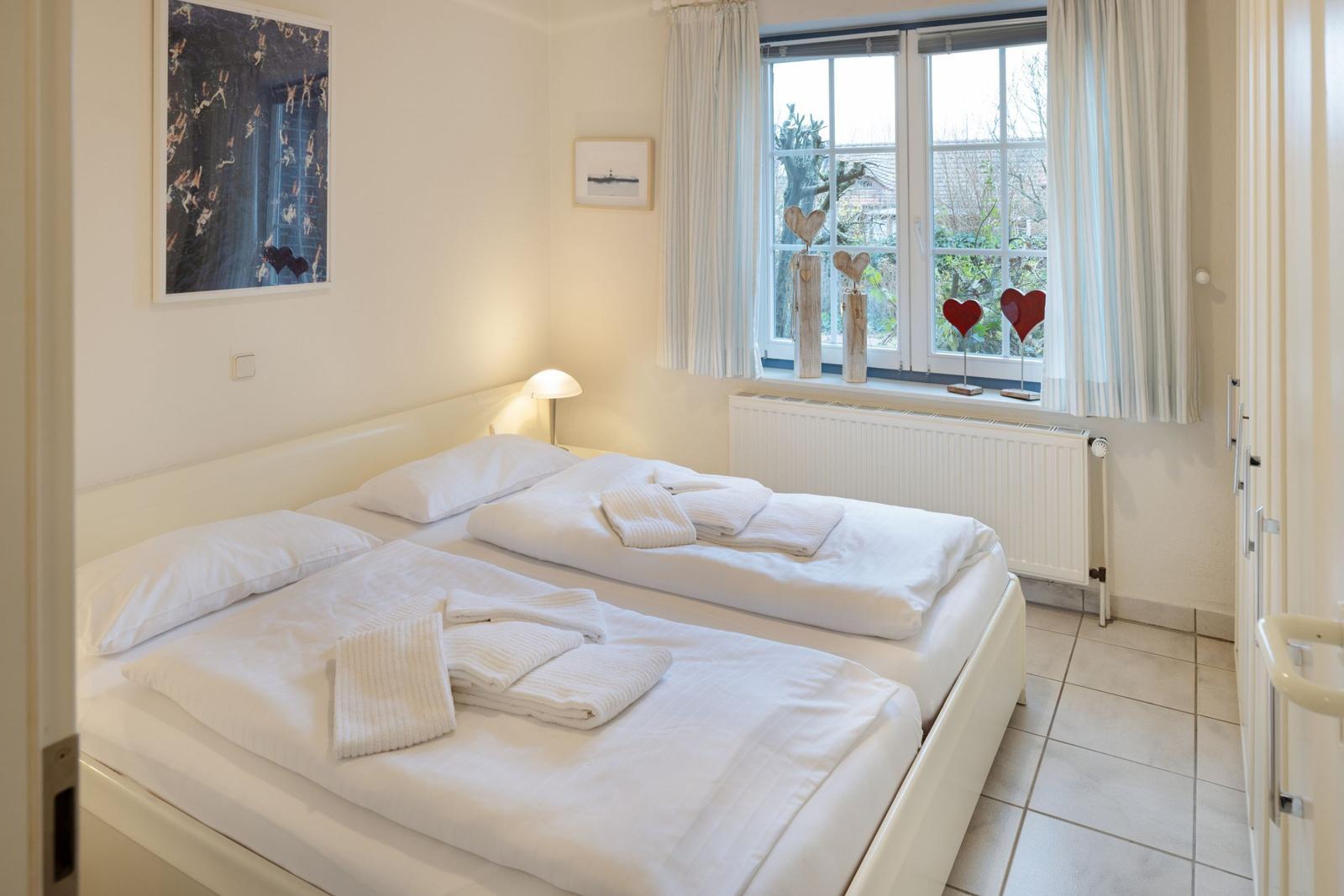 Schlafzimmer mit Doppelbett, Fenster und weißen Wänden.