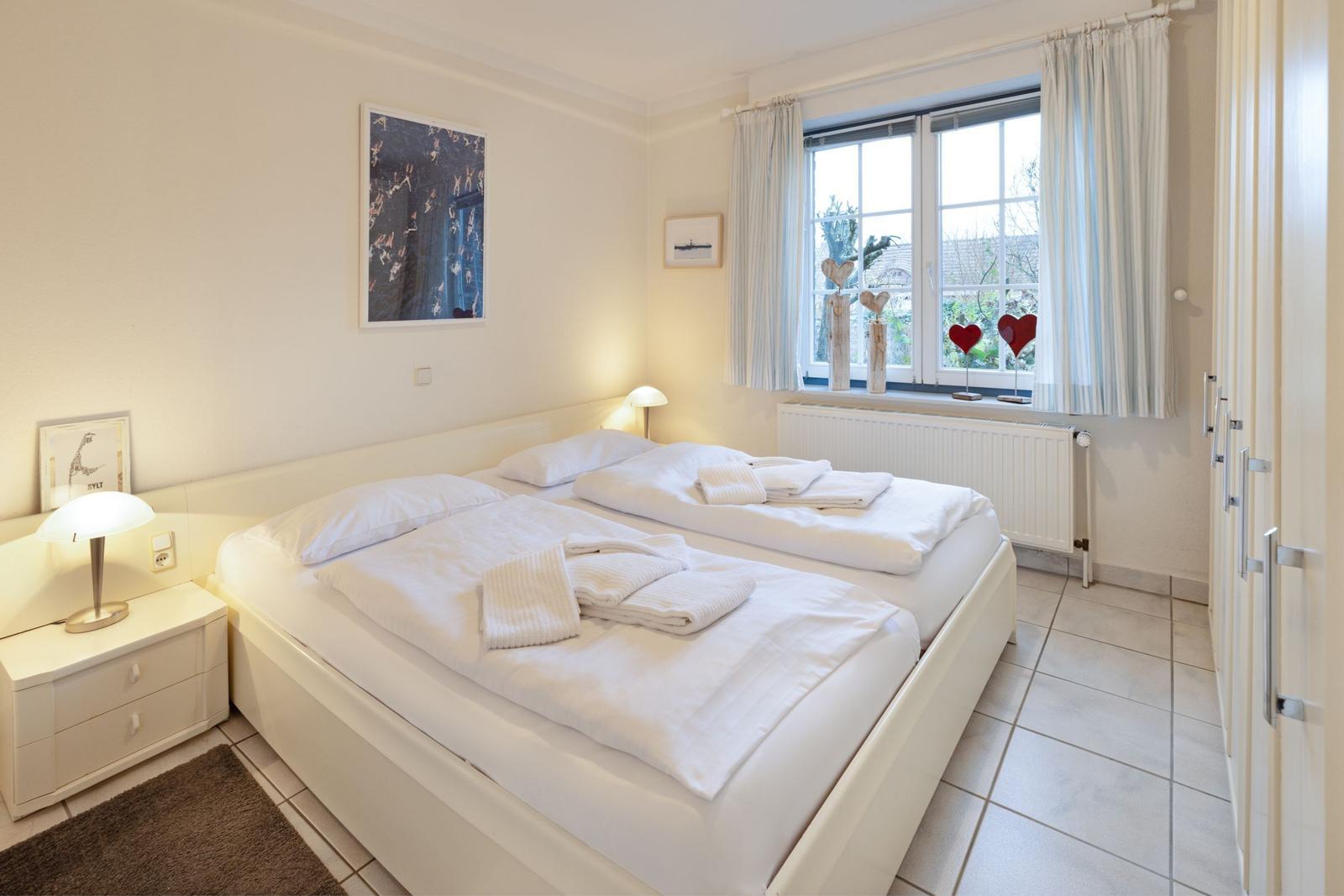 Ein Schlafzimmer mit Doppelbett, Nachttisch und Fenster mit Vorhängen.