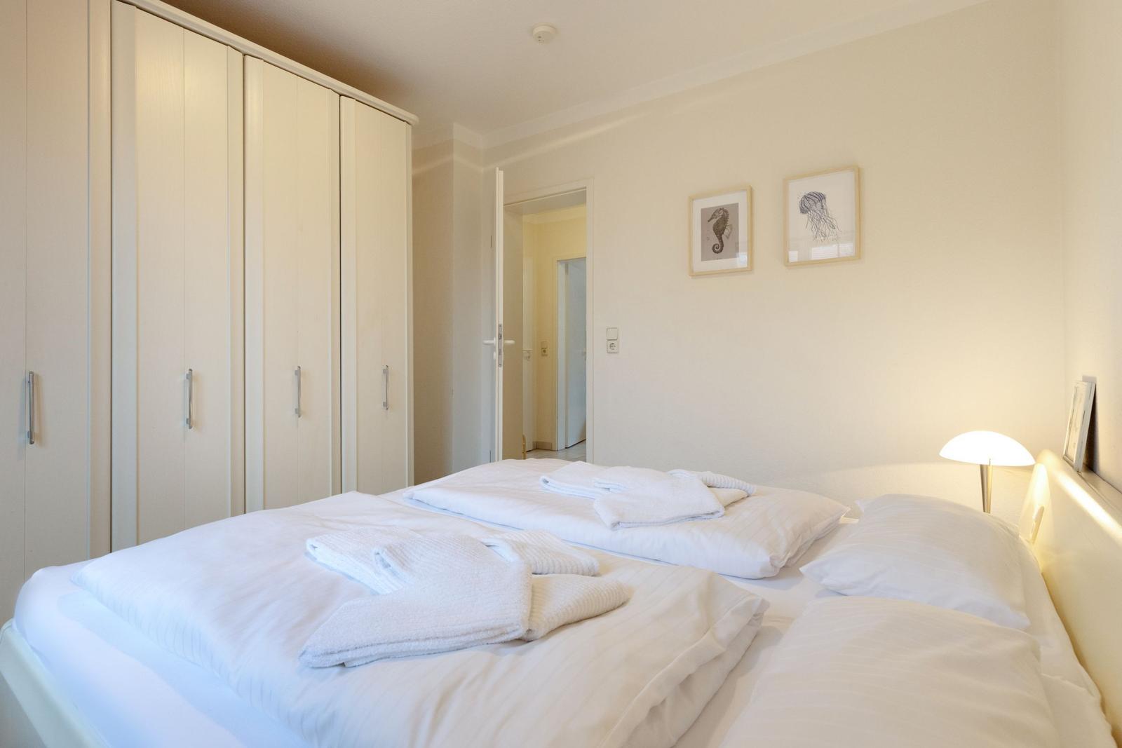 Schlafzimmer mit Bett, Kleiderschrank und Wandbildern.