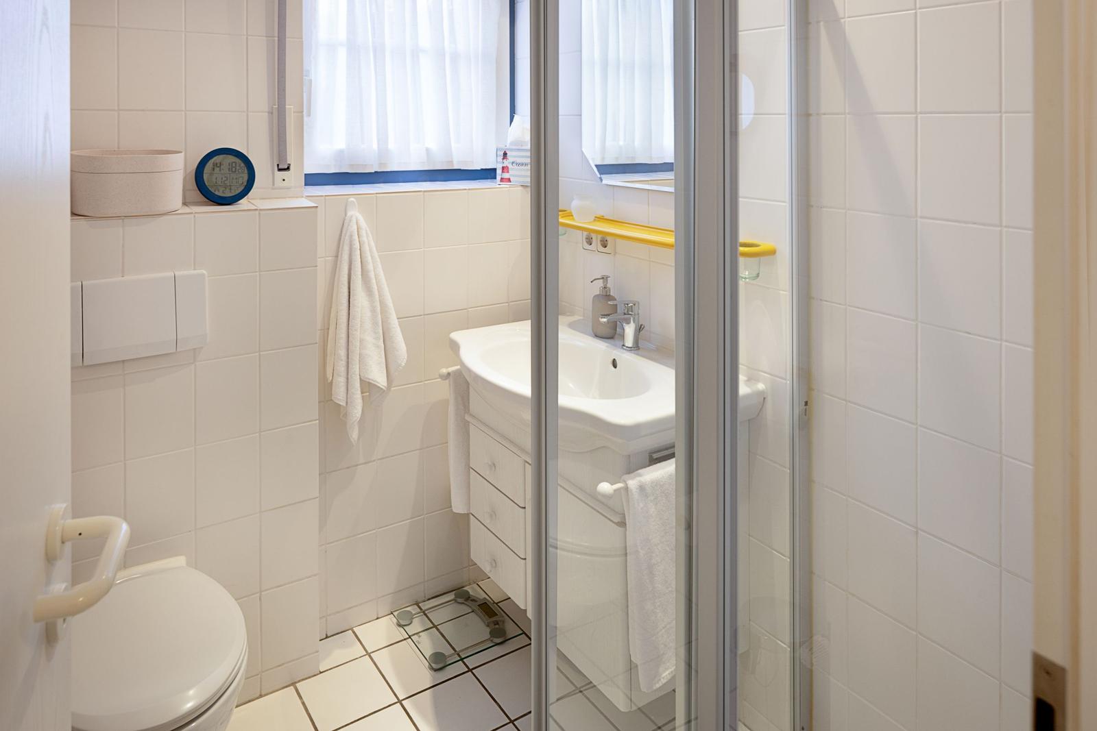 Badezimmer mit Toilette, Waschbecken und Dusche. Weiße Fliesen und Handtuchhalter.