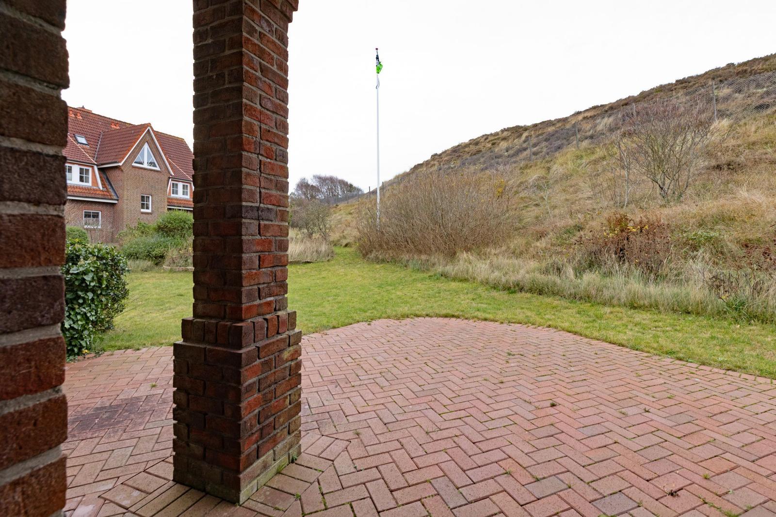 Hinterhof mit Steinplatten, Blick auf grünen Rasen und Hang.