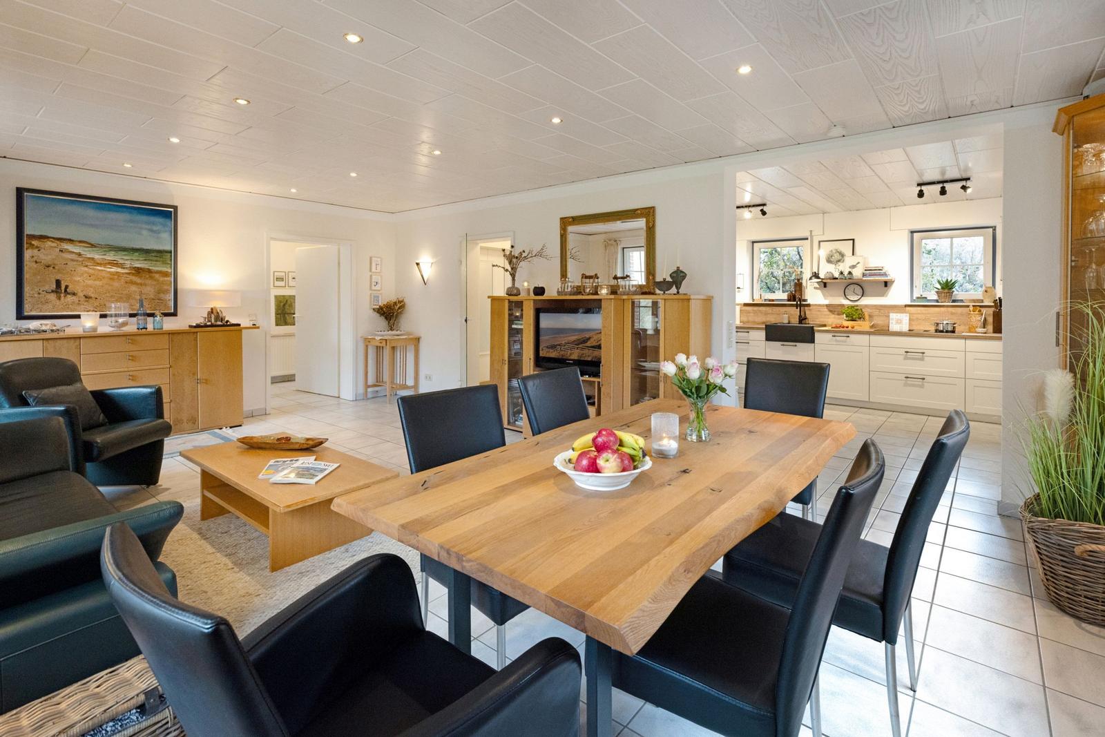Esszimmer mit Holztisch und schwarzen Stühlen. Küche und Wohnbereich sind sichtbar.