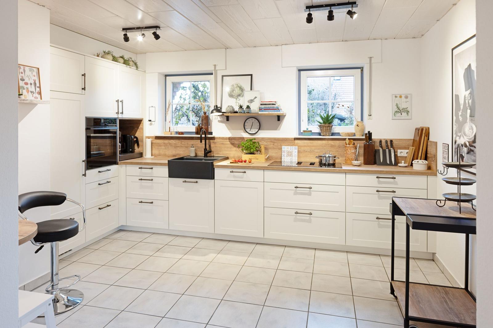 Moderne Küche mit weißen Schränken, Holzoberflächen und Fenstern mit Blick nach draußen.