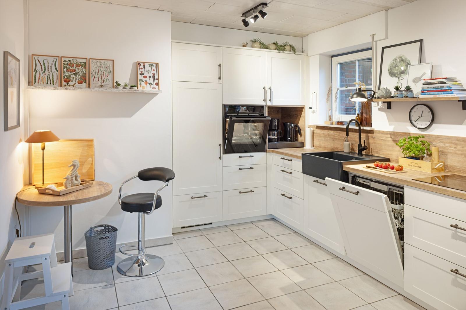 Küche mit weißen Schränken, Arbeitsfläche aus Holz, Spüle und integriertem Ofen.