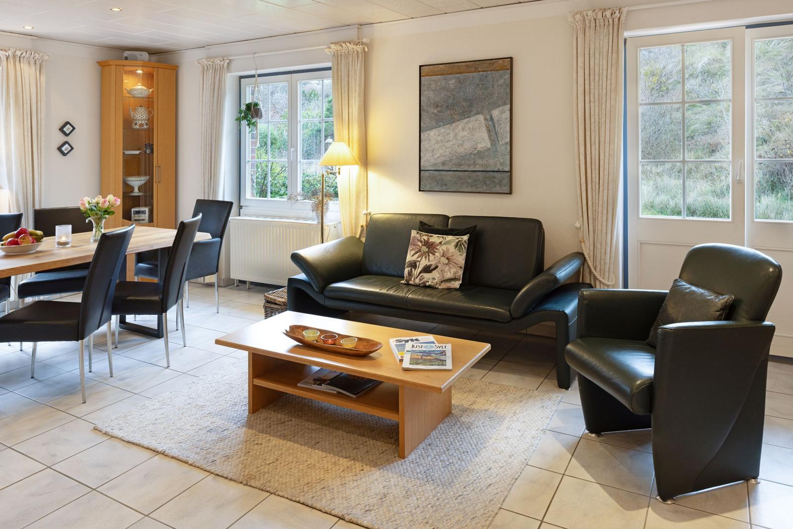 Wohn- und Essbereich mit Sofa, Stuhl, Tisch und Fenstern.