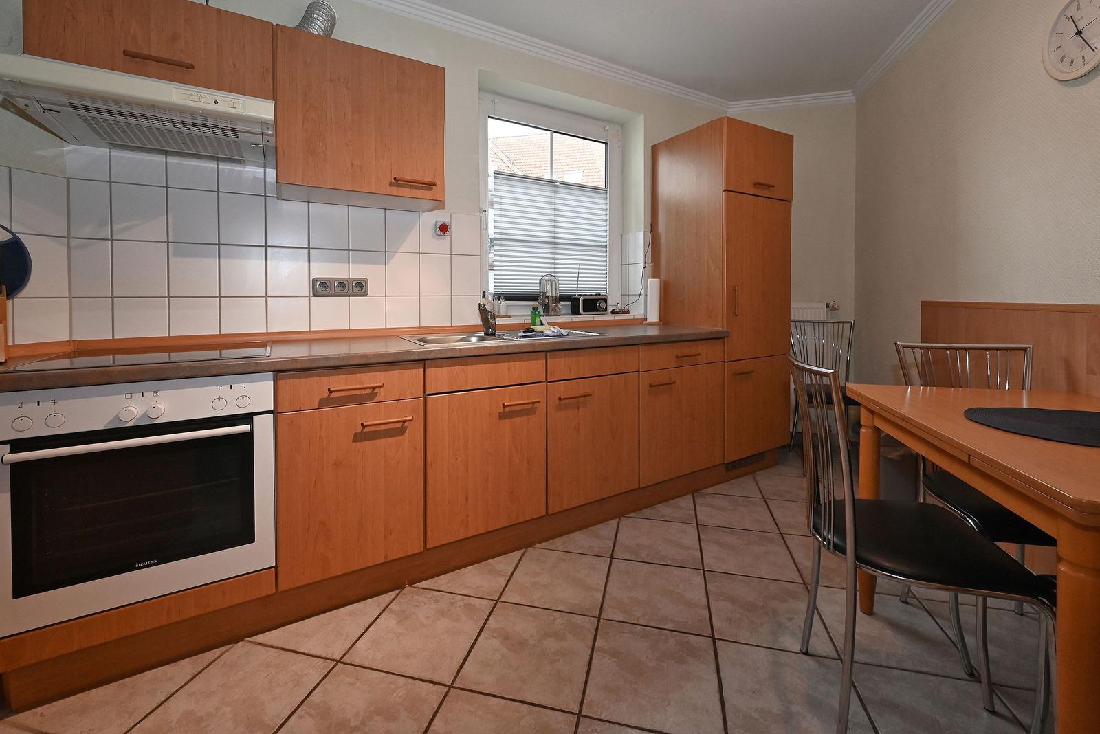 Küche mit Holzschränken, Spüle und Esstisch mit Stühlen.