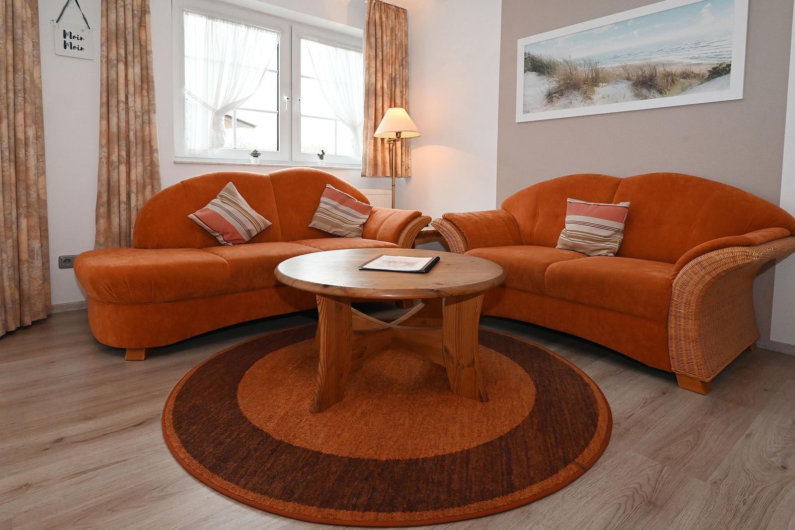 Ein Wohnzimmer mit zwei orangefarbenen Sofas, einem runden Holztisch und einem runden Teppich.