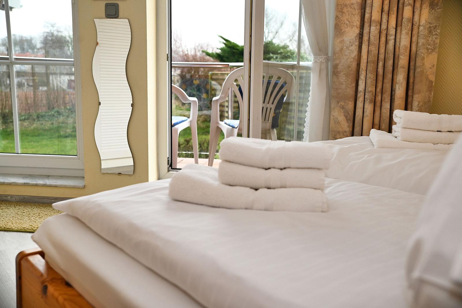 Schlafzimmer mit Bett, Handtüchern und Blick auf Balkon mit Stühlen.