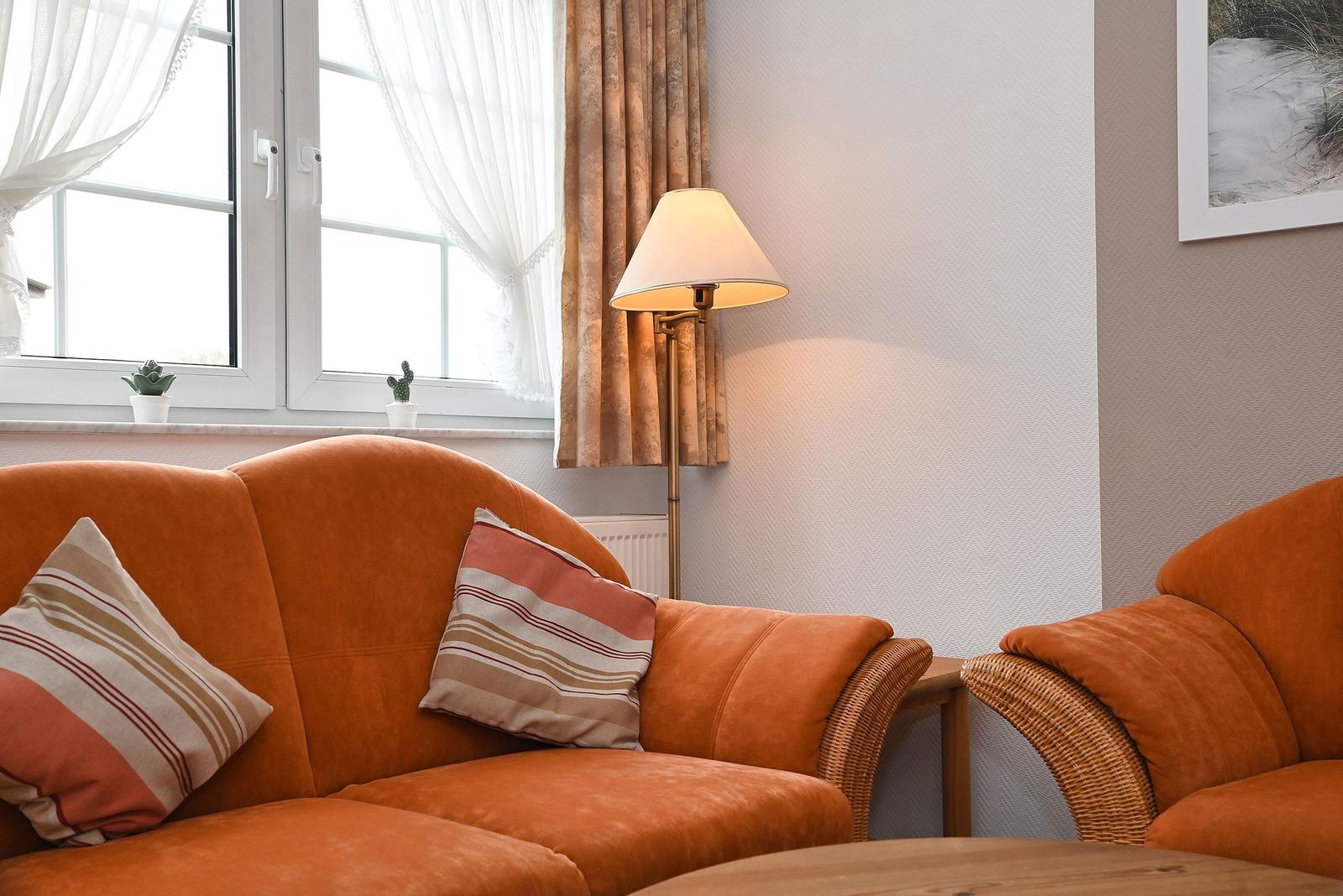 Ein Wohnzimmer mit orangefarbenem Sofa, Stehlampe und Fenster mit Vorhängen.
