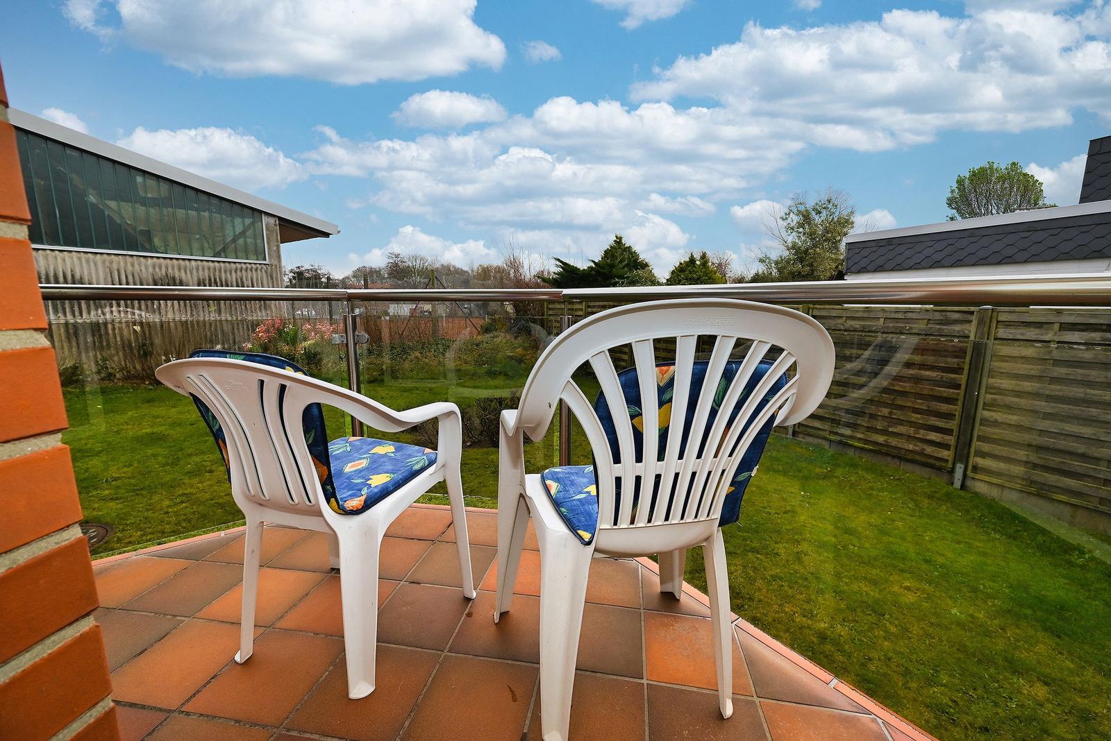 Terrasse mit zwei weißen Stühlen und blauen Sitzkissen. Blick auf grünen Garten und Himmel.