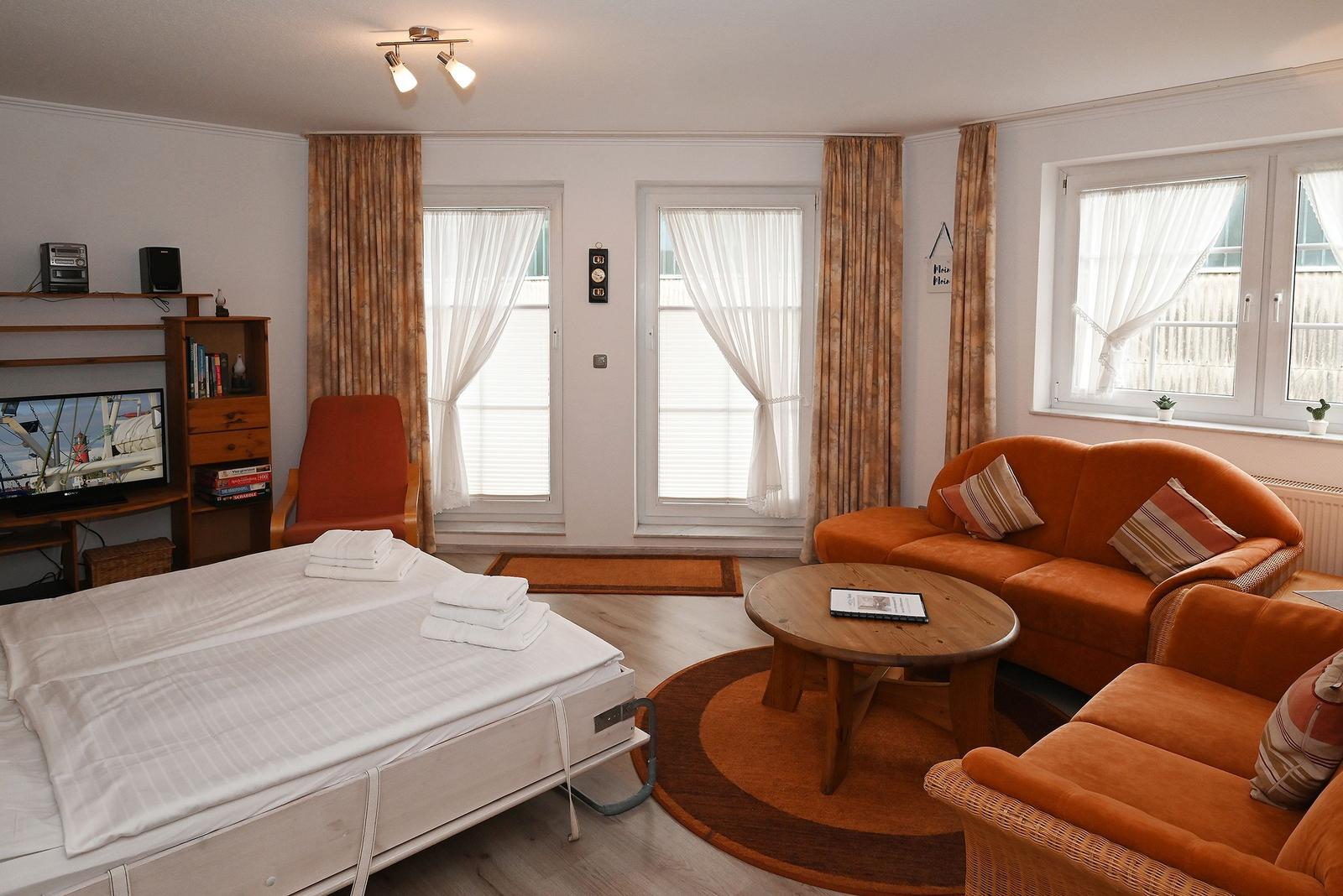 Schlafzimmer mit Bett, Sofa, Fernseher und Fenstern mit Vorhängen.