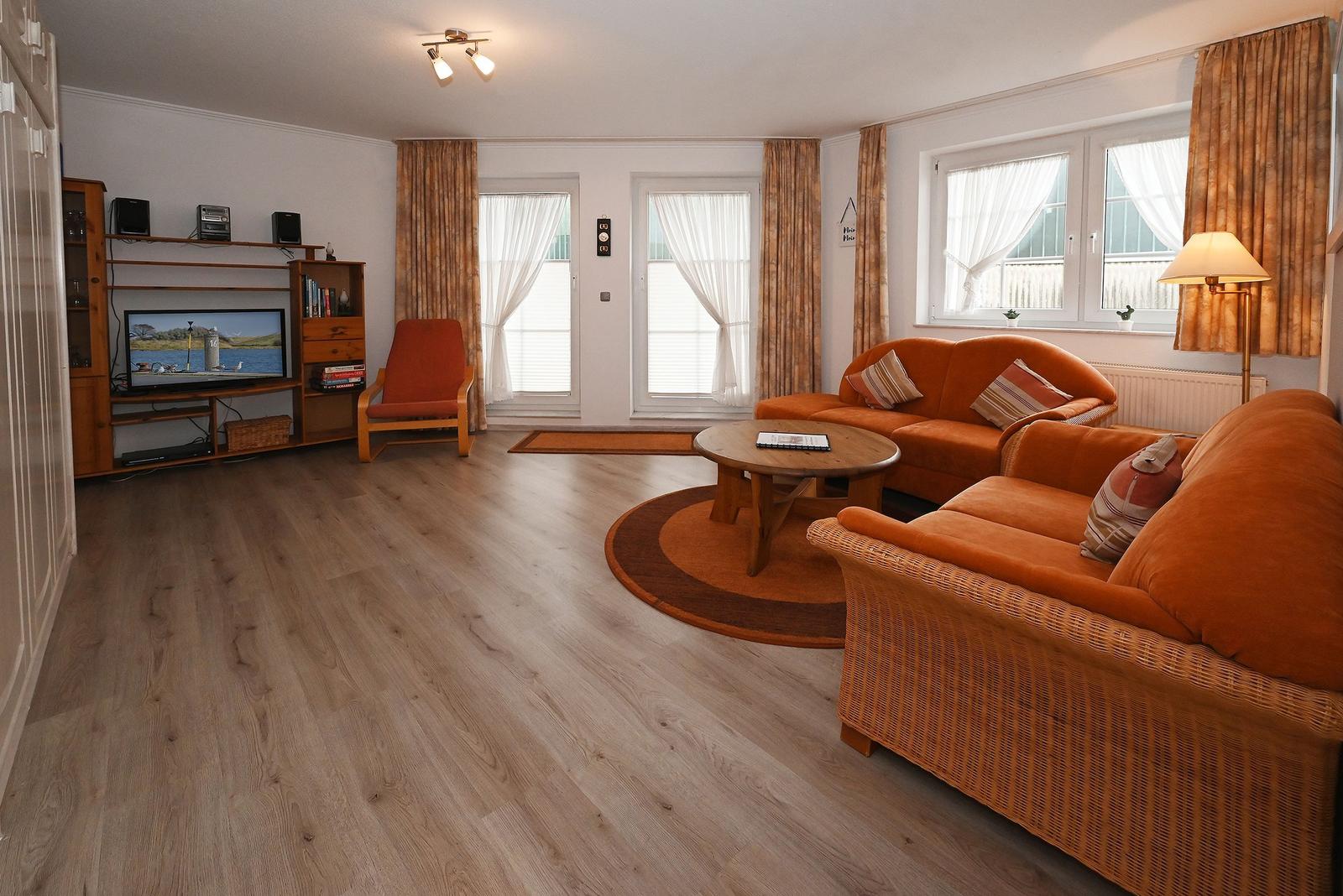 Wohnzimmer mit orangefarbenen Sofas, Holzboden und Fernseher.