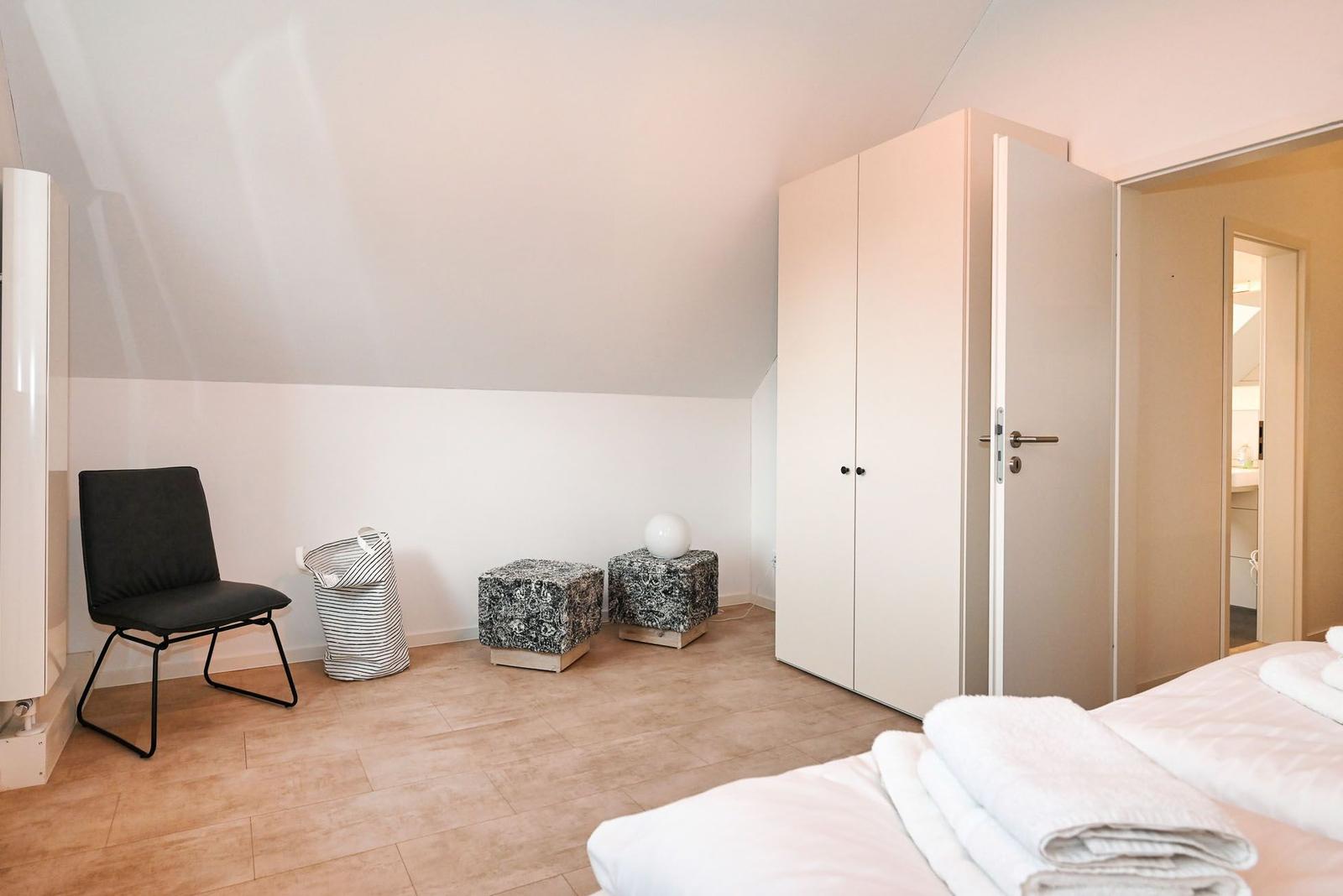 Schlafzimmer mit Bett, Kleiderschrank und Stuhl. Durchgang zur Badewanne.